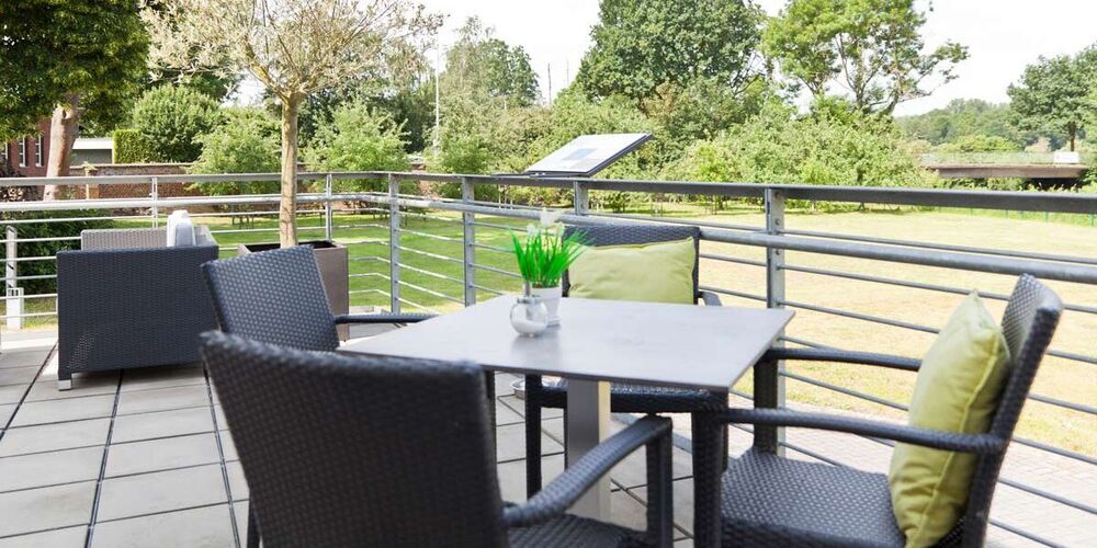 Terrasse des Haus St. Martinus. Auf dieser stehen Tische mit Stühlen. Im Hintergrund befindet sich die Gartenanlage.