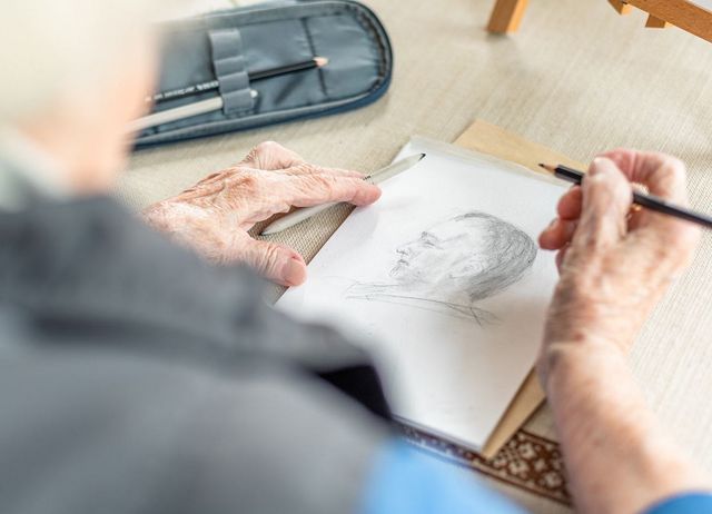 Eine ältere Person zeichnet mit einem Bleistift einen Mann im Profil.